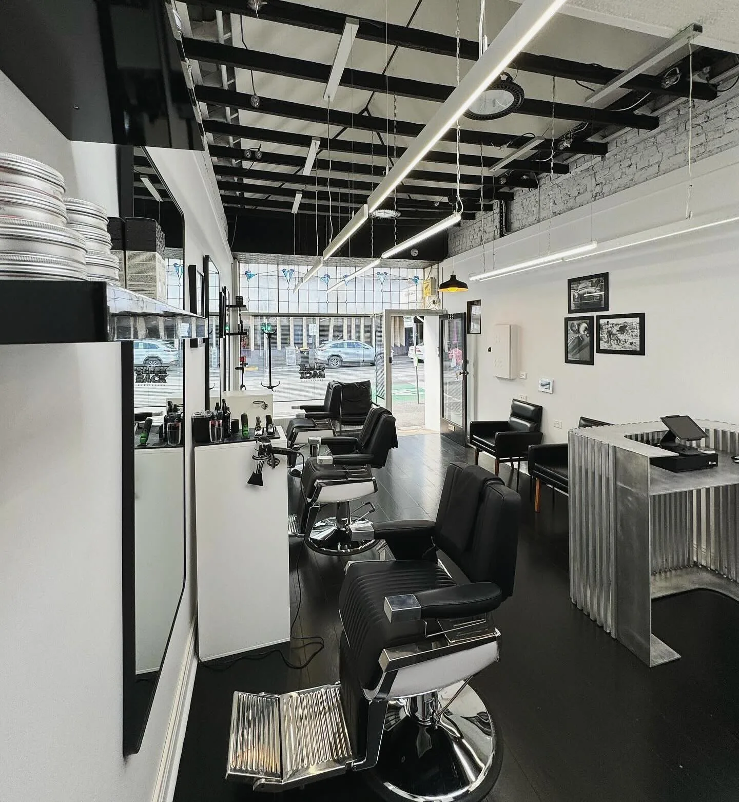Sleek Back Barbershop interior — full row of chrome barber chairs to the street window, exposed beams, B&W fit-out