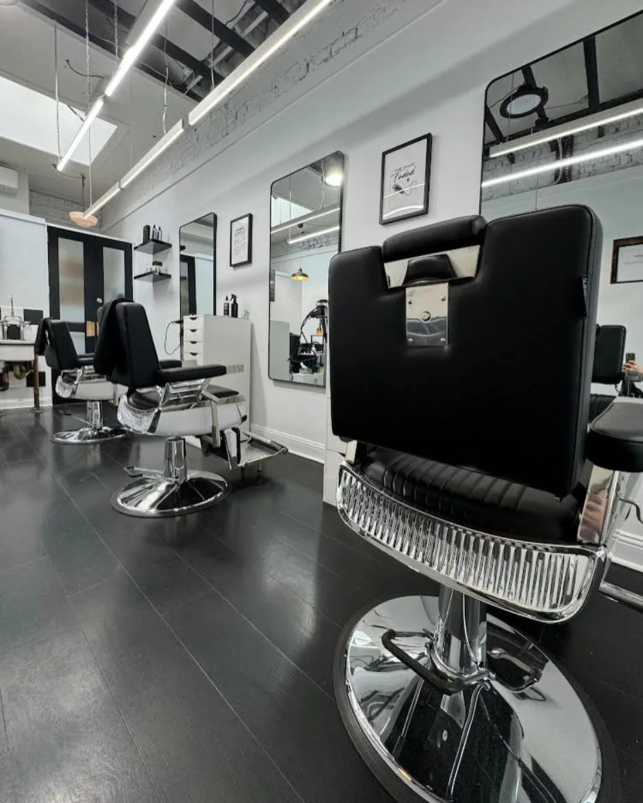 Barbershop interior — two barber chairs, framed 'Time to get faded' print, black floor, white brick