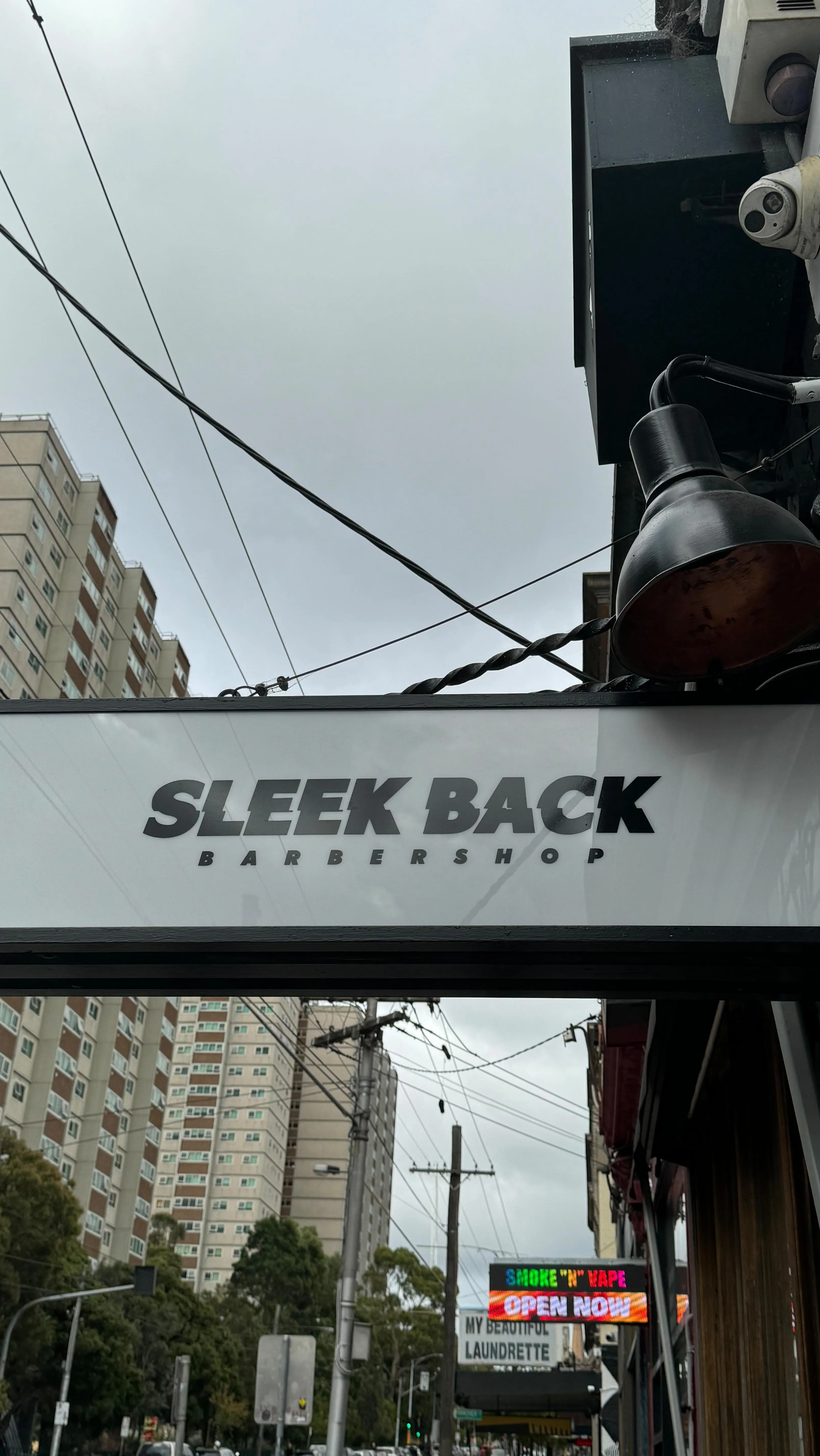 Sleek Back Barbershop exterior blade sign, Brunswick Street Fitzroy — Atherton Gardens towers behind