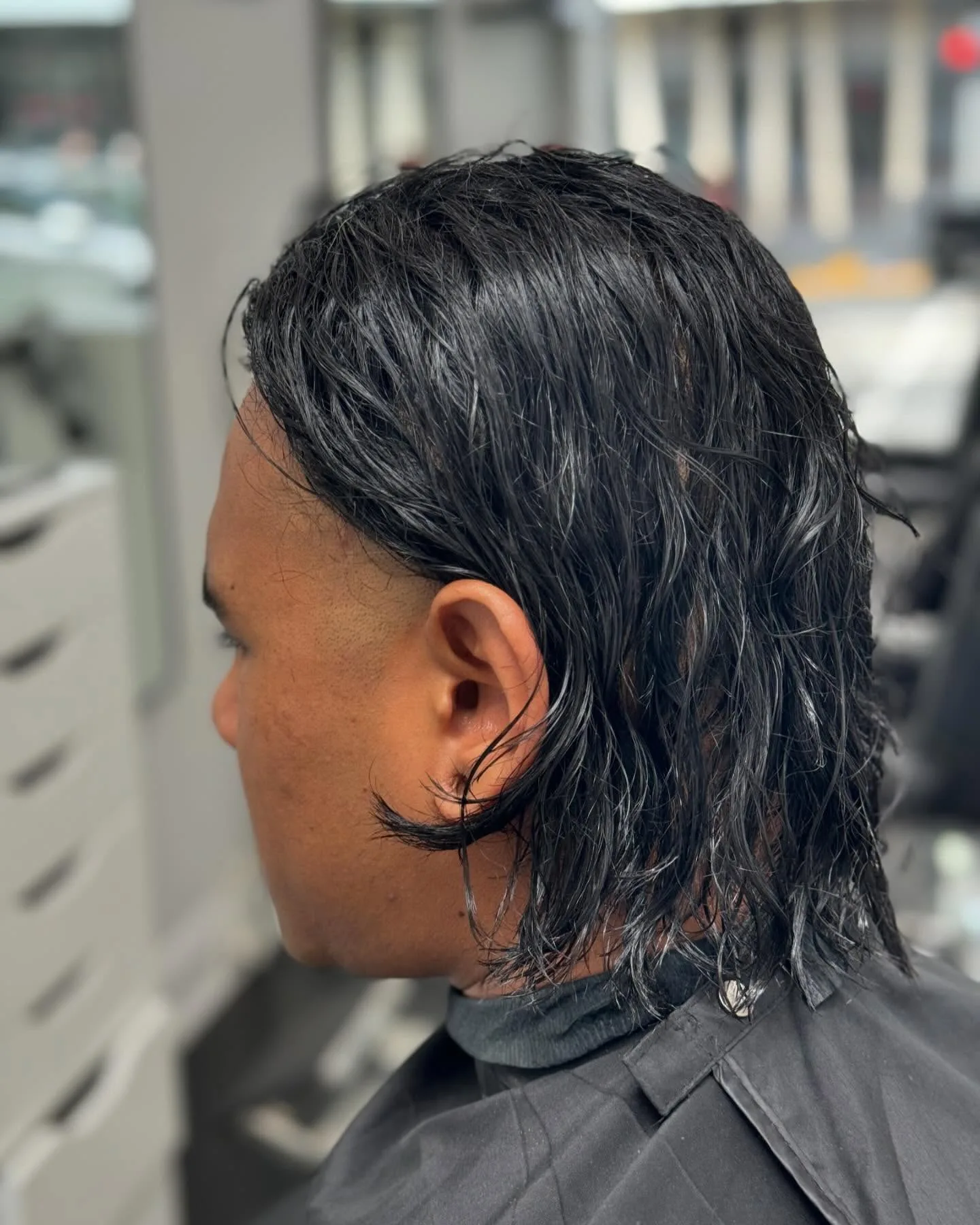 Long wavy mullet-length cut, side profile, salon window behind