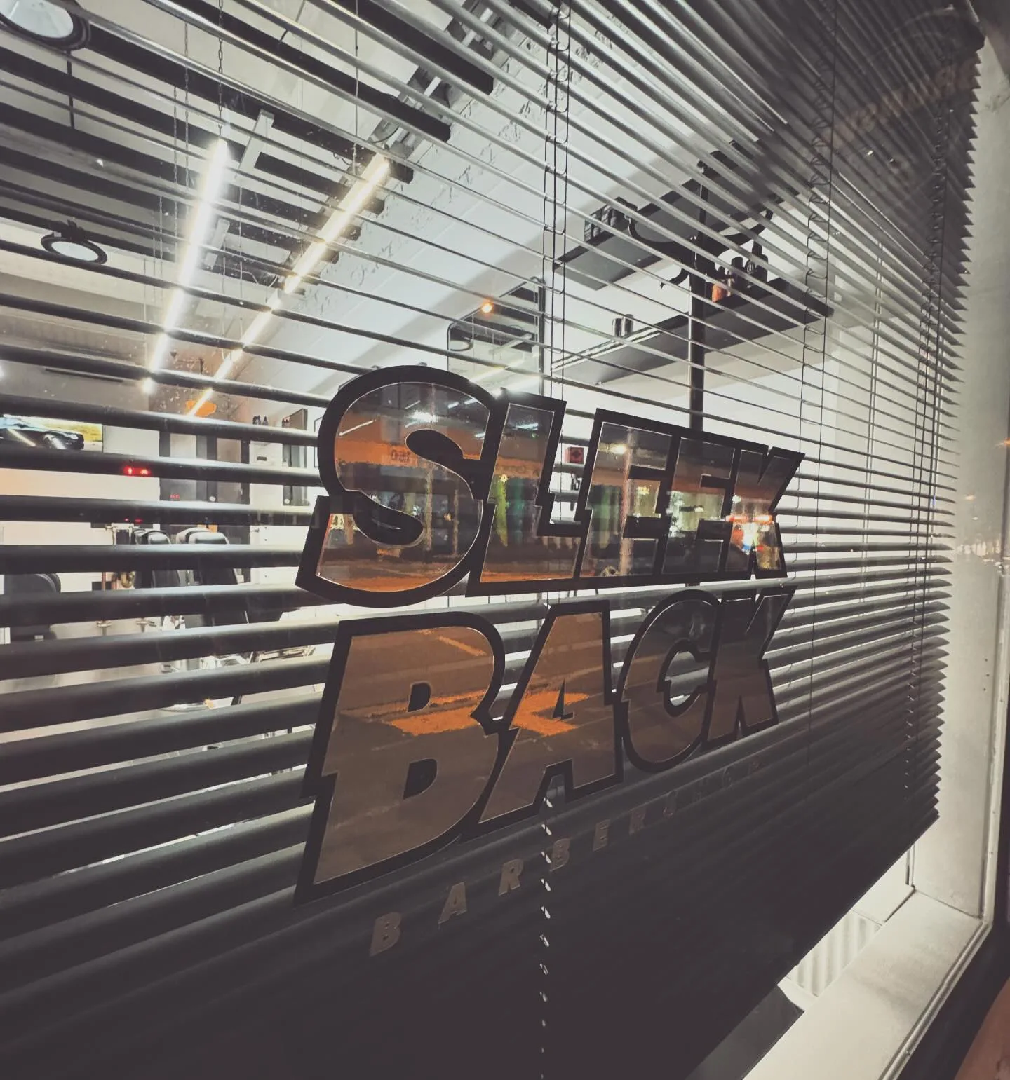 Sleek Back Barbershop night shopfront — SLEEK BACK BARBERSHOP window decal, warm interior glow